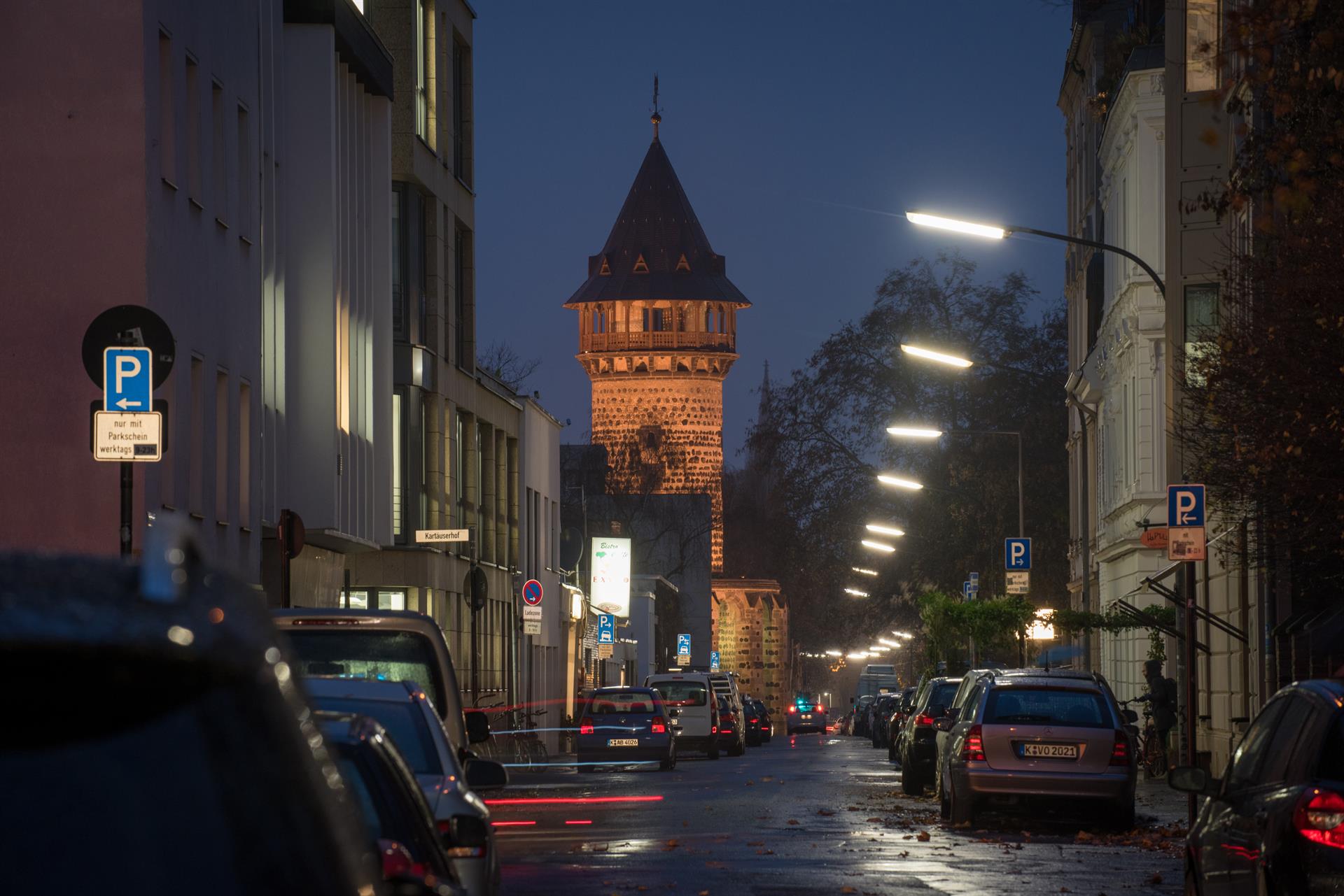 Eine Kölner Straße bei nächtlicher Straßenbeleuchtung, mit der Ulrepforte im Hintergrund