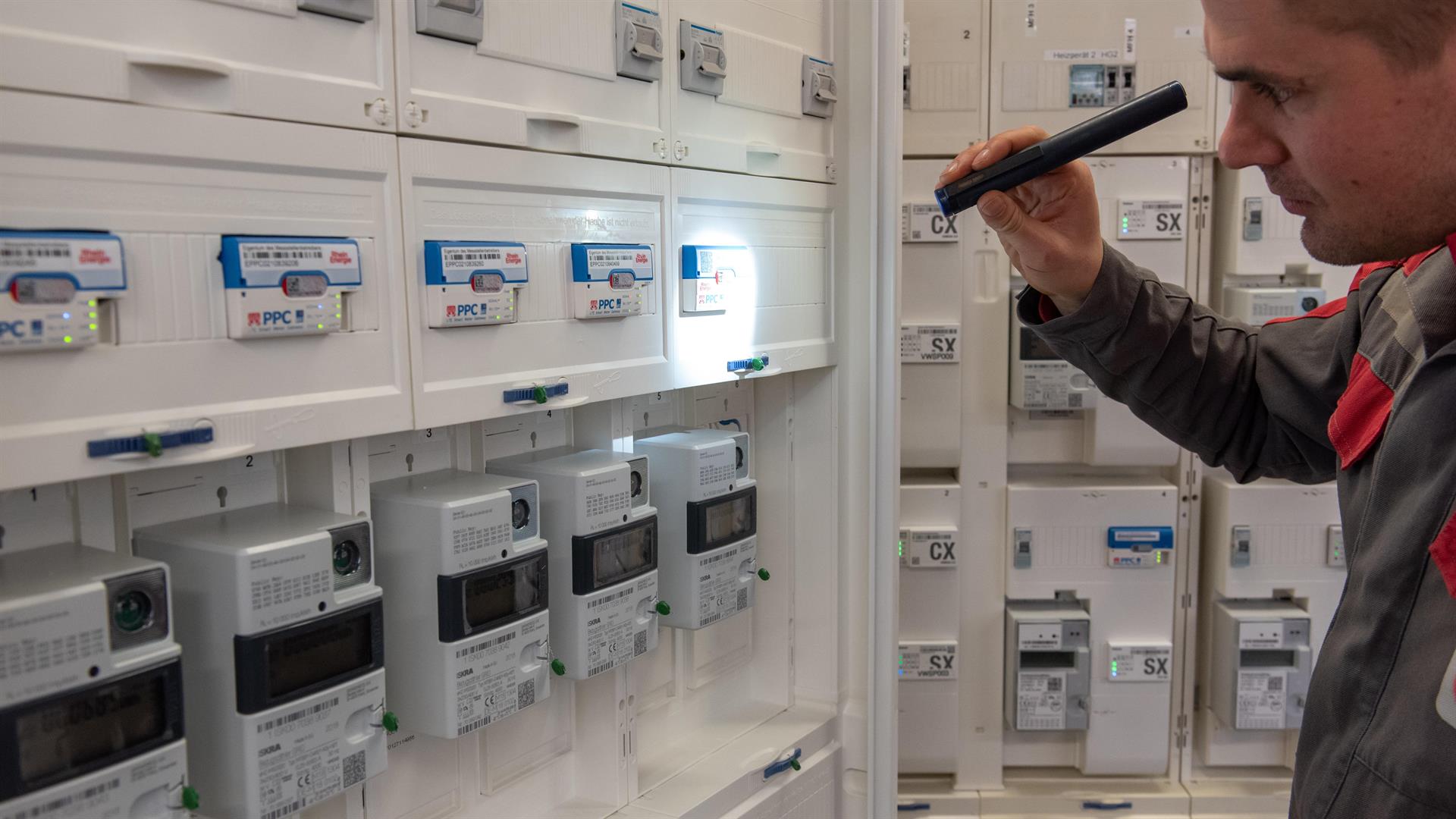 Ein RheinNetz-Mitarbeiter leuchtet mit einer Taschenlampe in eine Zähleranlage auf ein Smart Meter Gateway